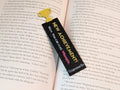 Black rectangle bookmark with a yellow trophy icon on one end. Yellow text on the bookmark reads "NEW ACHIEVEMENT!". Text below in white reading "Wow. You can read.". Magenta text reads "Whoopie."